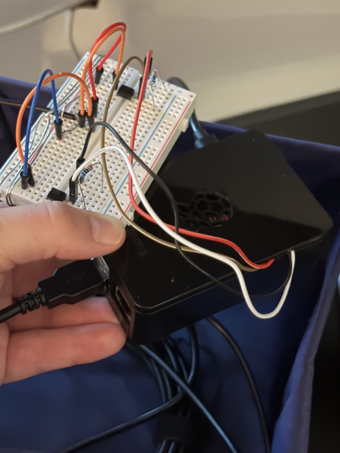A breadboard of jumper wires and components held in one hand, wired to a Raspberry Pi in a black case